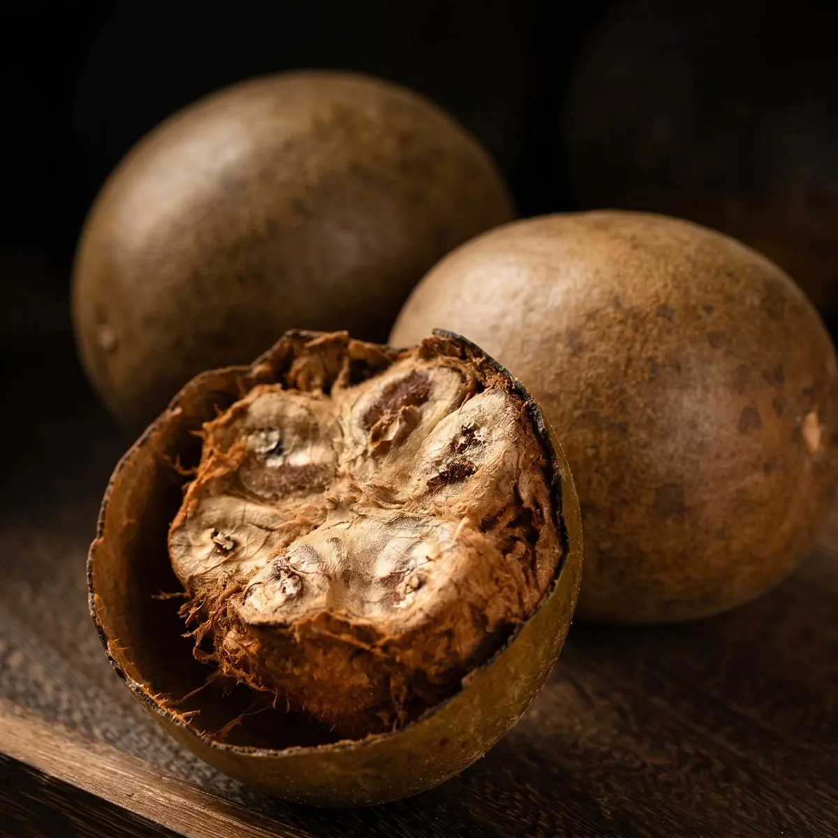 Two whole dried monk fruits beside one broken open, showing the pale fibrous flesh inside